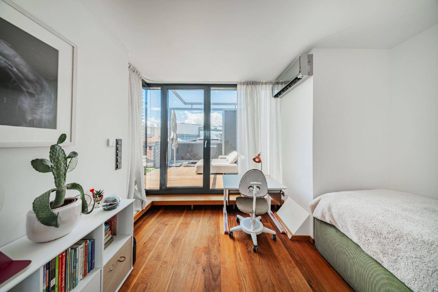 Helles Schlafzimmer mit Holzboden, Schreibtisch und Zugang zu einer Außenterrasse.