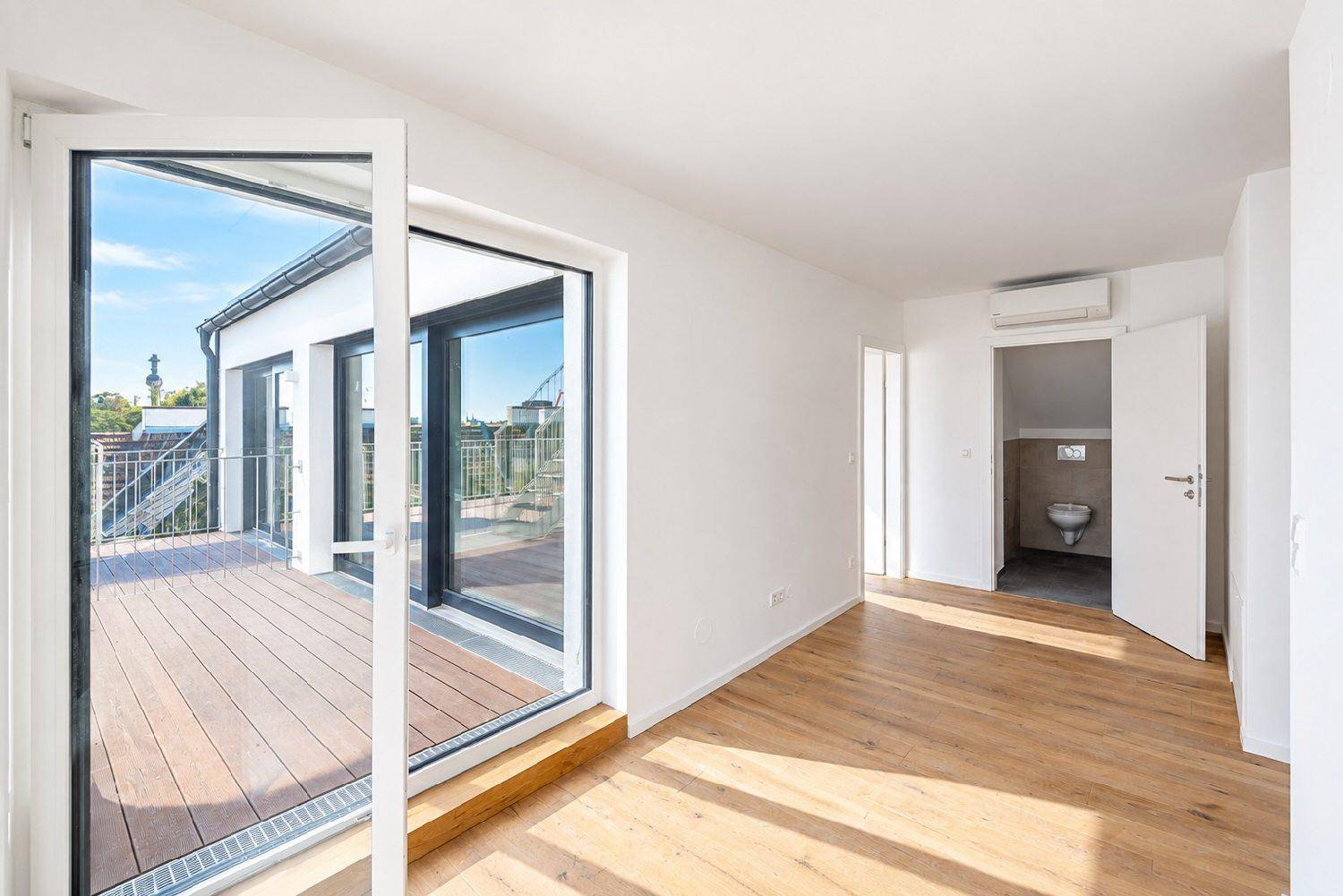 Geräumiger Innenraum mit Holzboden, Zugang zu einer Holzterrasse und Blick auf ein separates WC.