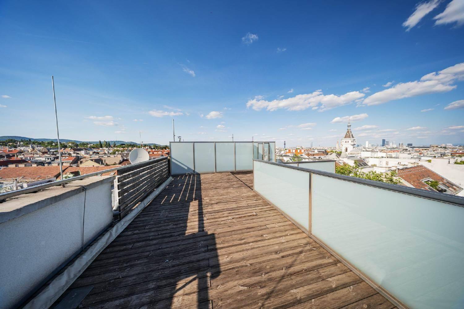 Weitläufige Dachterrasse mit Holzboden und Panoramablick über die Dächer der Stadt.