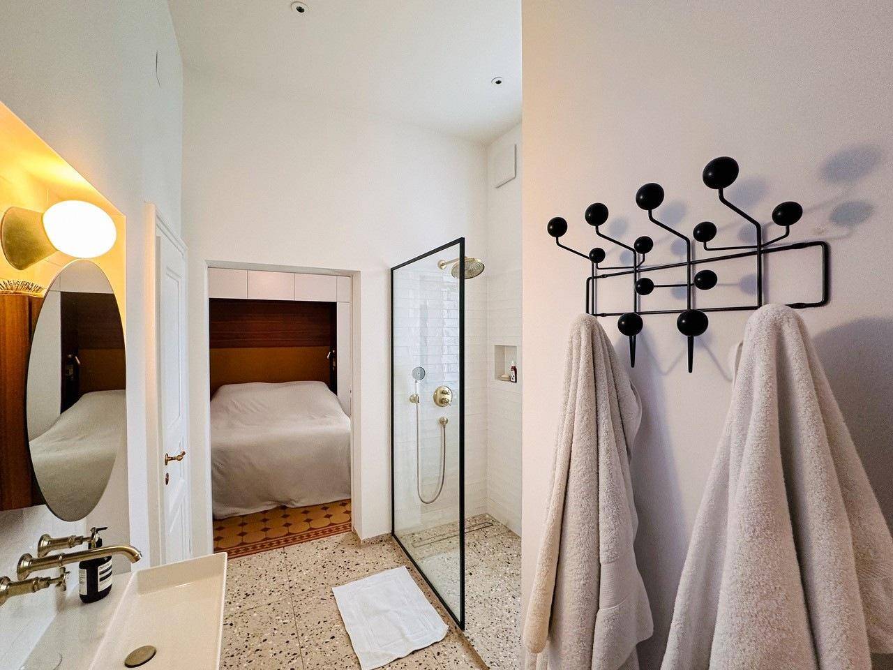Modernes Badezimmer mit begehbarer Dusche, Terrazzoboden und Blick ins Schlafzimmer.