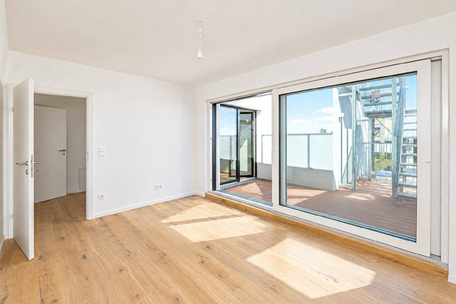 Heller Raum mit Holzboden und großer Schiebetür, die zu einer weitläufigen Holzterrasse führt.