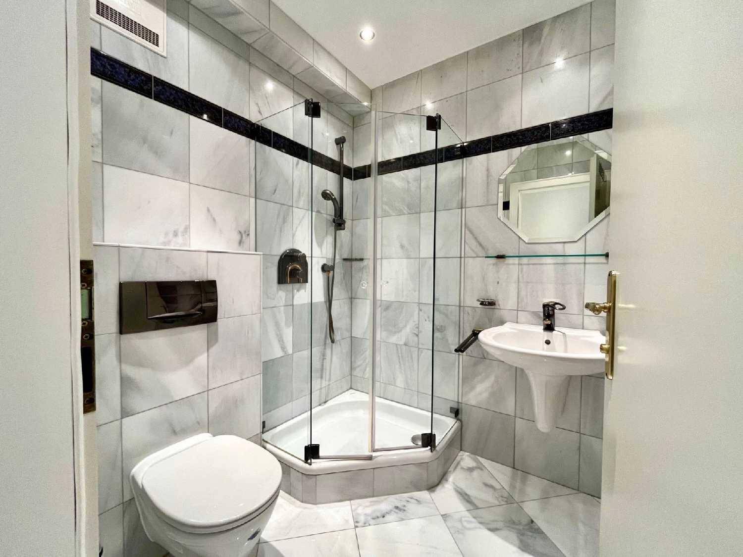 Kleines Badezimmer mit Dusche, WC und Waschbecken, komplett gefliest in Marmoroptik.