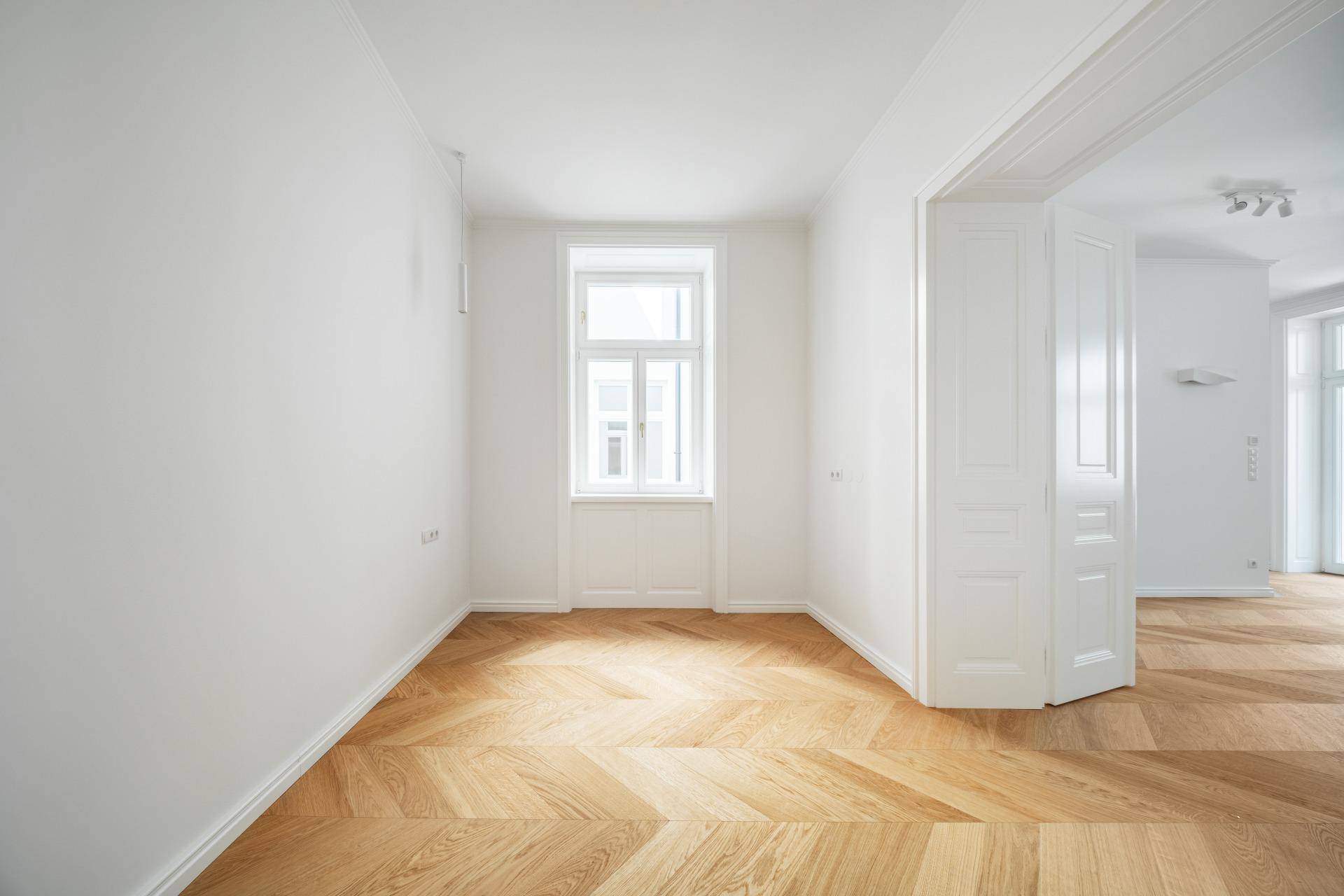 Ruhiges, helles Zimmer mit Fischgrätparkett und einem Fenster, ideal als Schlaf- oder Arbeitszimmer.