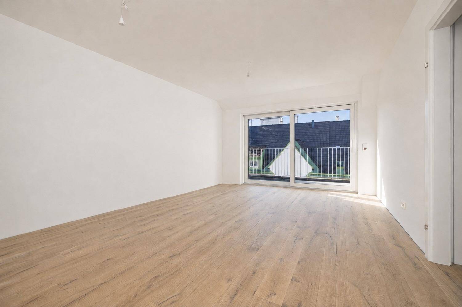 Heller, leerer Wohnraum mit großen Schiebetüren und Zugang zu einem Balkon.