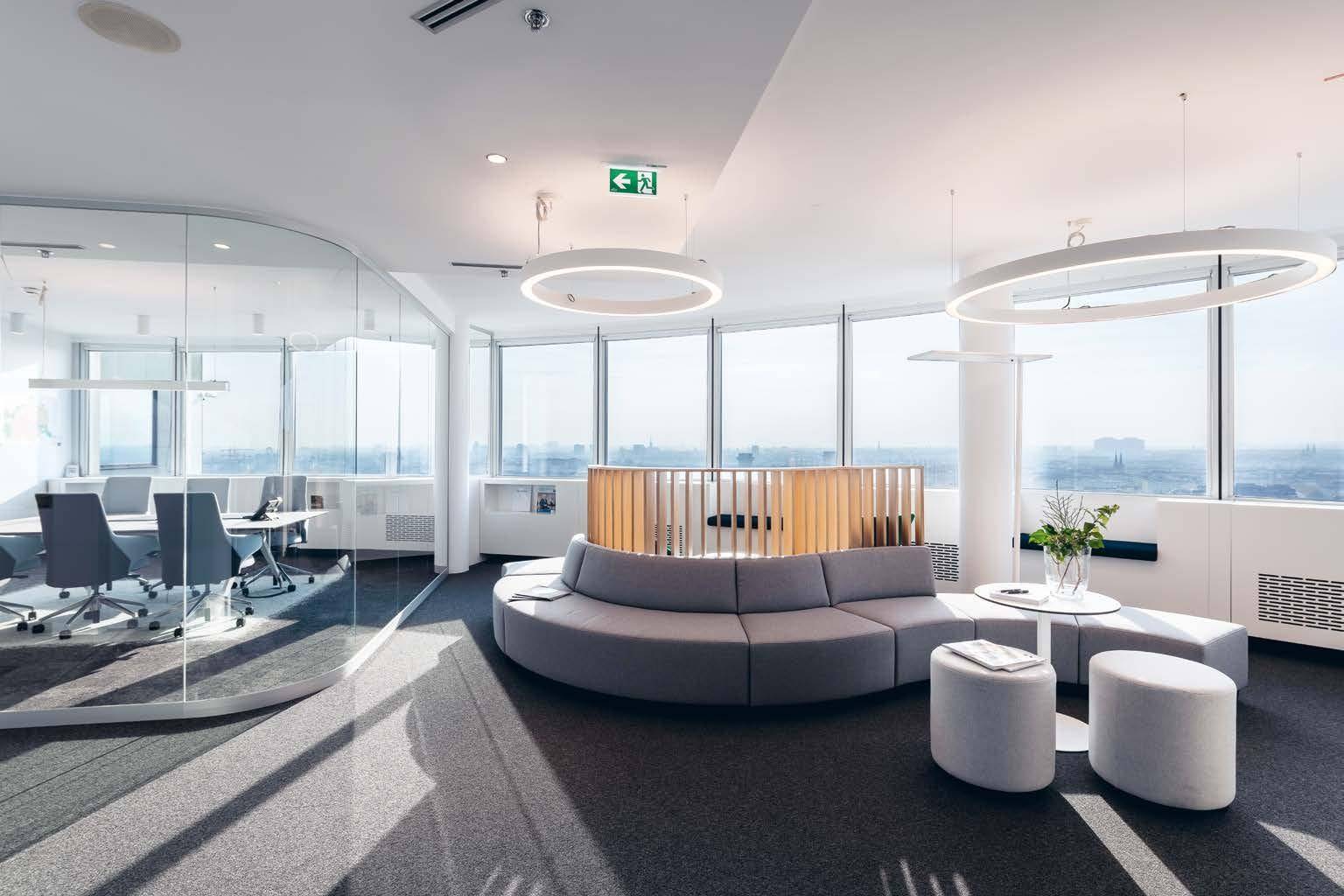 Heller Besprechungs- und Loungebereich mit Glaswänden, modernen Möbeln und Panoramablick auf die Stadt.