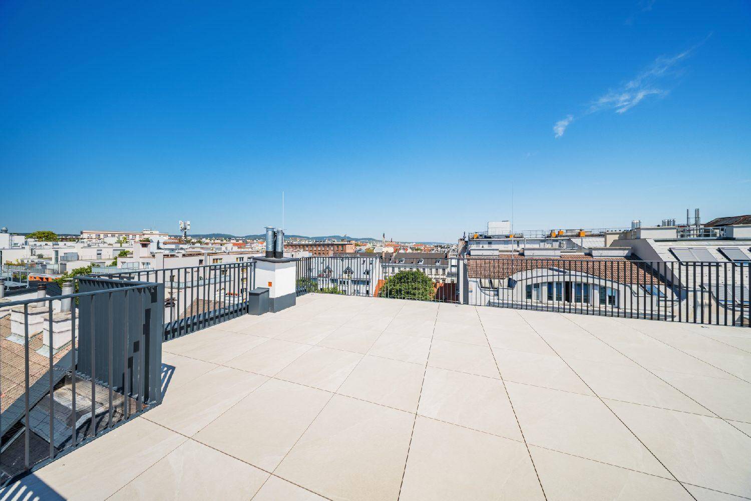 Weitläufige Dachterrasse mit Fliesenboden und Panoramablick über die Dächer der Stadt.