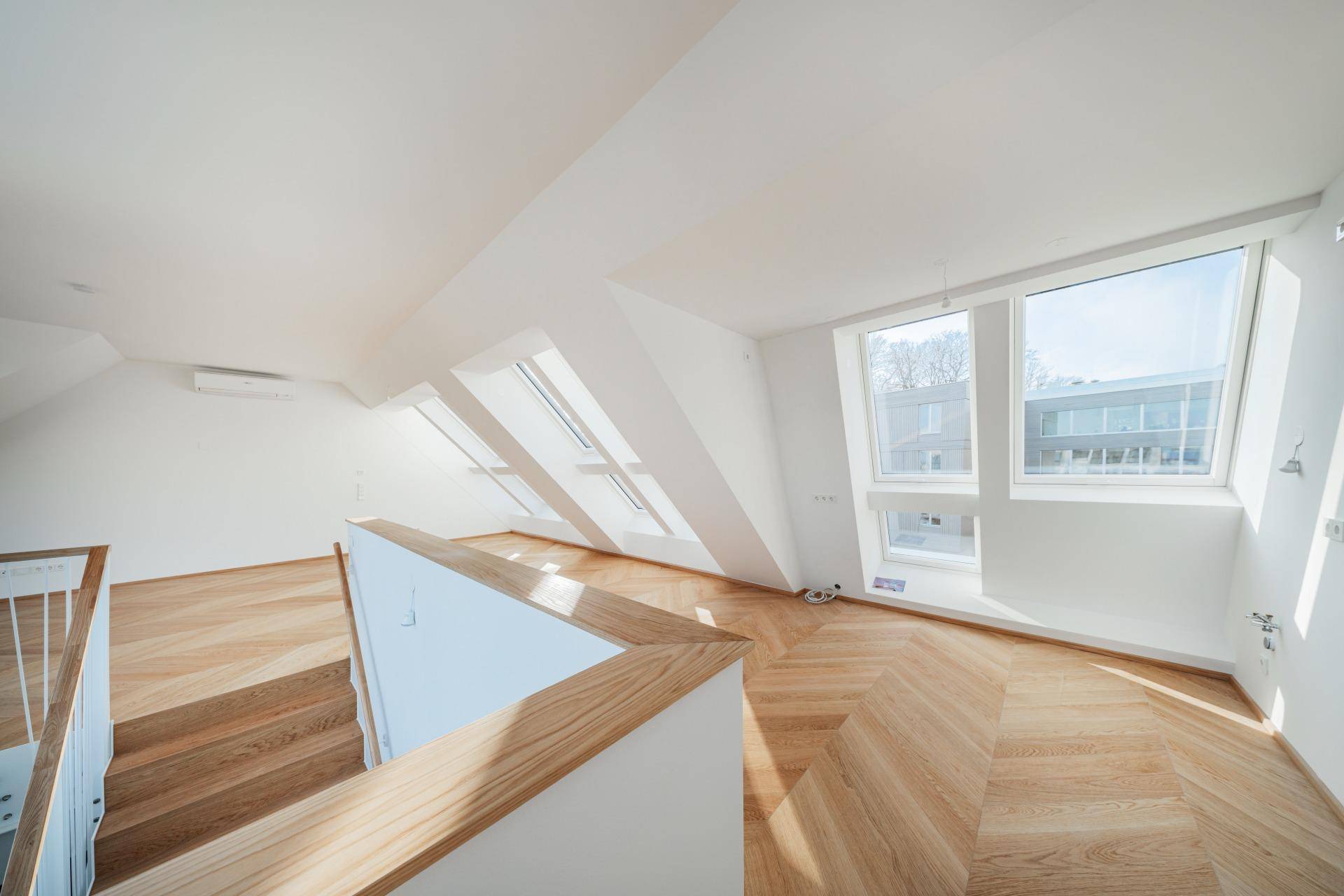 Lichtdurchfluteter Wohnbereich im Dachgeschoss mit vielen Fenstern und Blick auf das Treppenhaus.