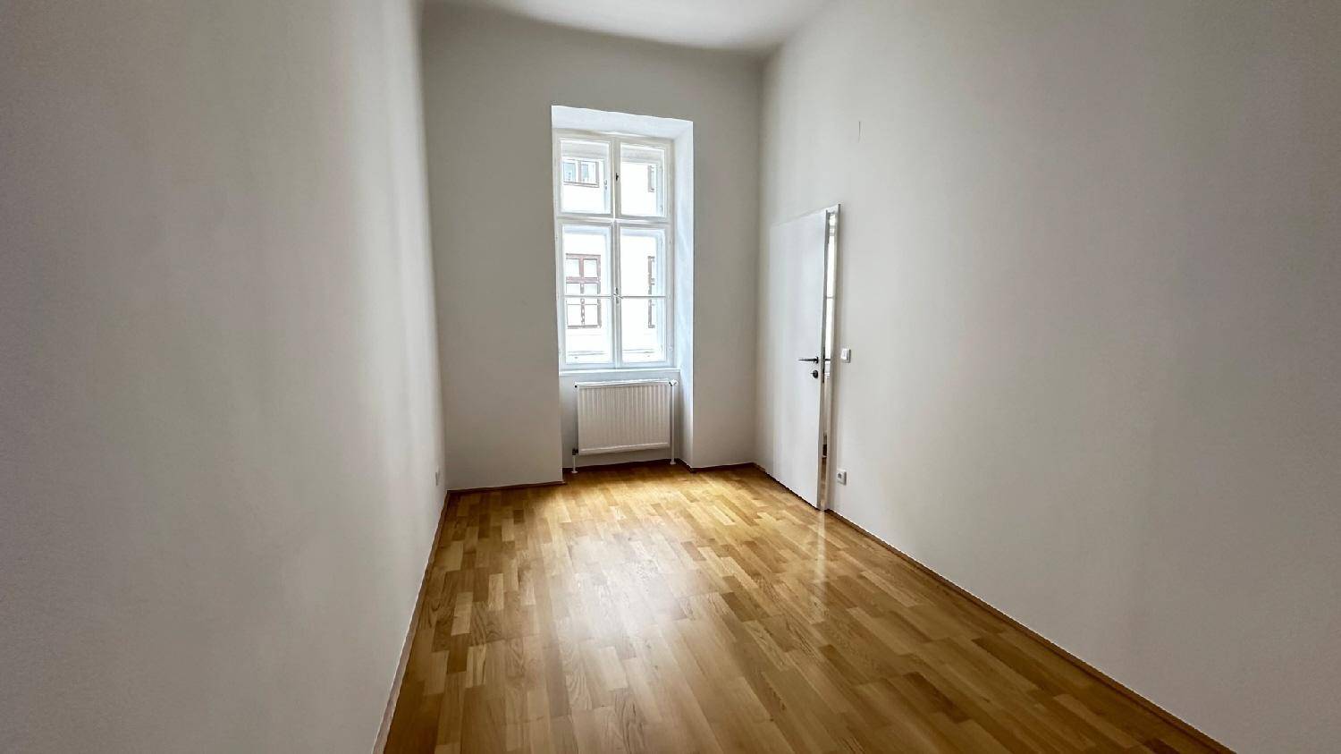 Ruhiges Zimmer mit Parkettboden und einem großen Fenster, ideal als Schlaf- oder Arbeitszimmer nutzbar.