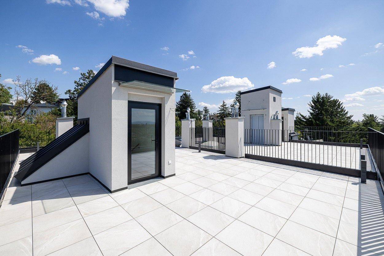 Weitläufige Dachterrasse mit modernen Fliesen und kleinen Gebäuden, umgeben von viel Grün.