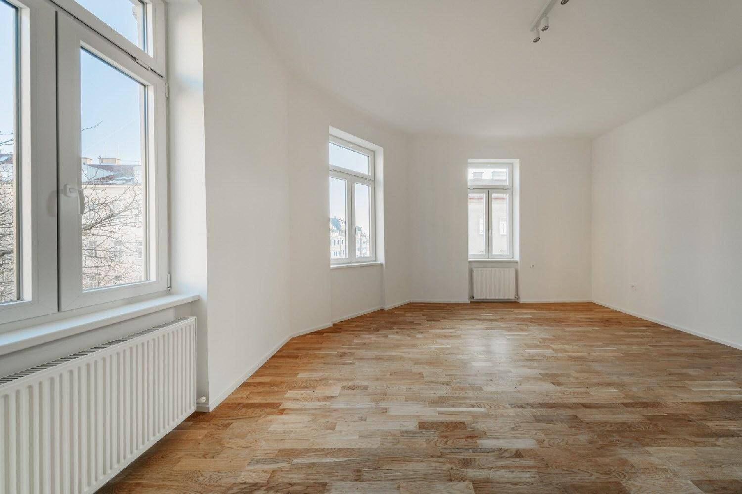 Geräumiges, helles Zimmer mit Holzboden und mehreren Fenstern, die eine gute Belichtung bieten.