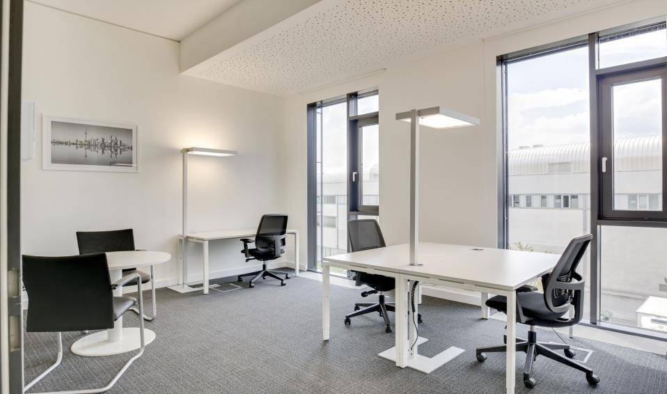 Helles Einzelbüro mit modernen Schreibtischen, Bürostühlen und großen Fenstern mit Stadtblick.