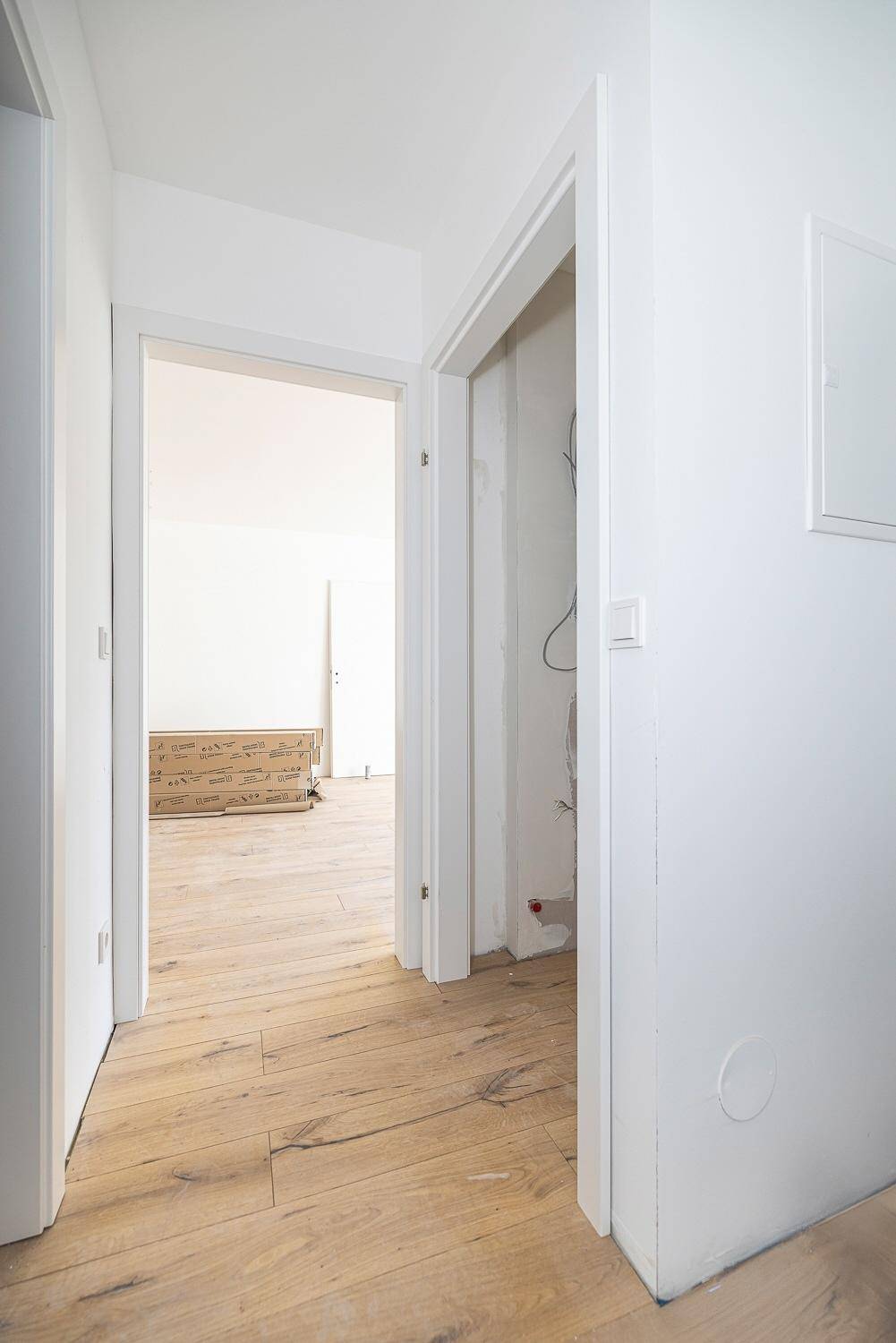 Heller Flur im Neubau mit Holzboden und offenen Türen zu angrenzenden Räumen.