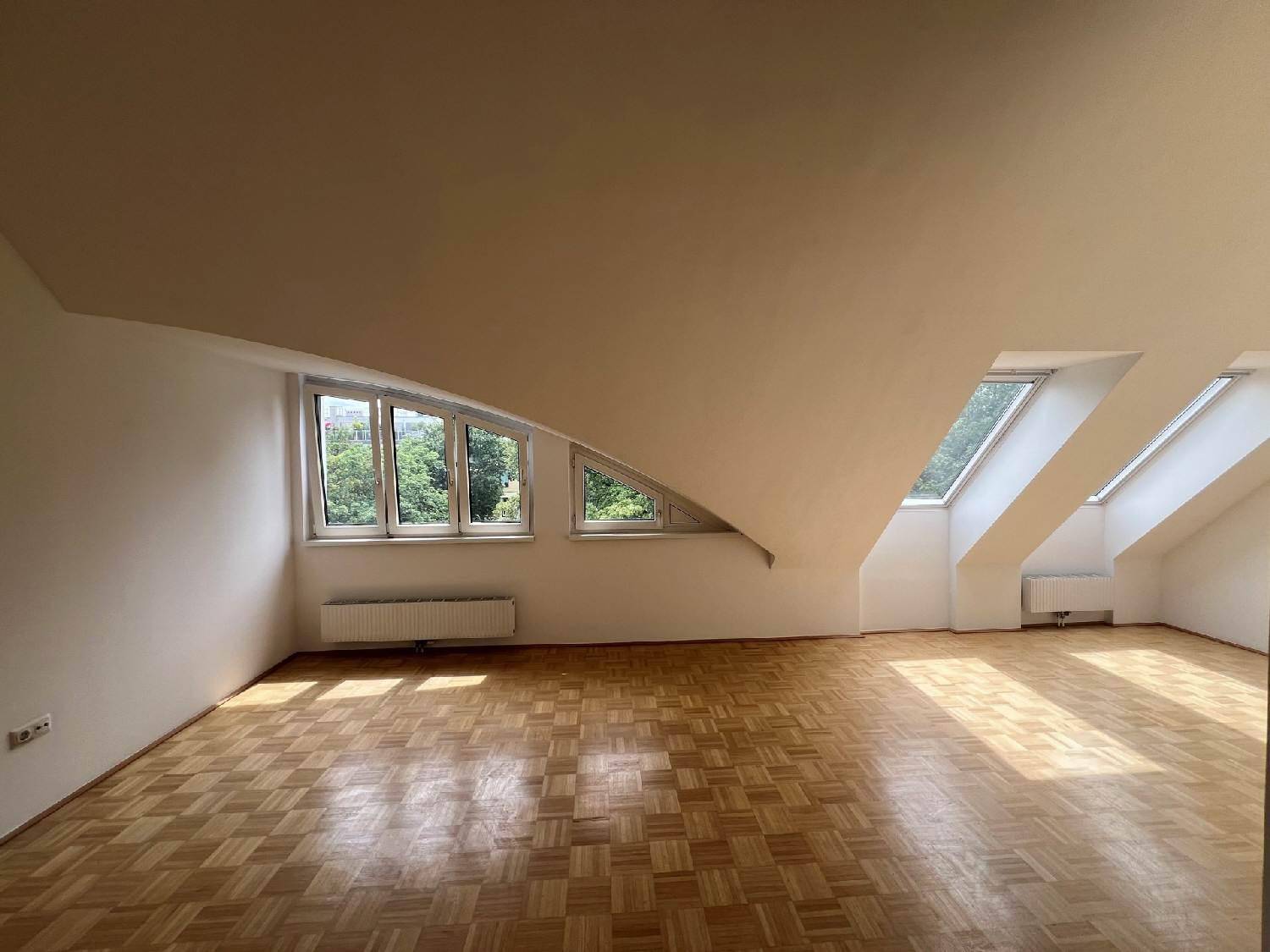Lichtdurchflutetes Zimmer mit Parkettboden, Dachschrägen und mehreren Dachfenstern.