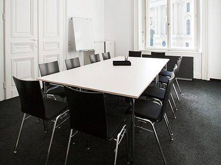 Heller Konferenzraum mit großem Tisch, schwarzen Stühlen und Blick nach draußen.