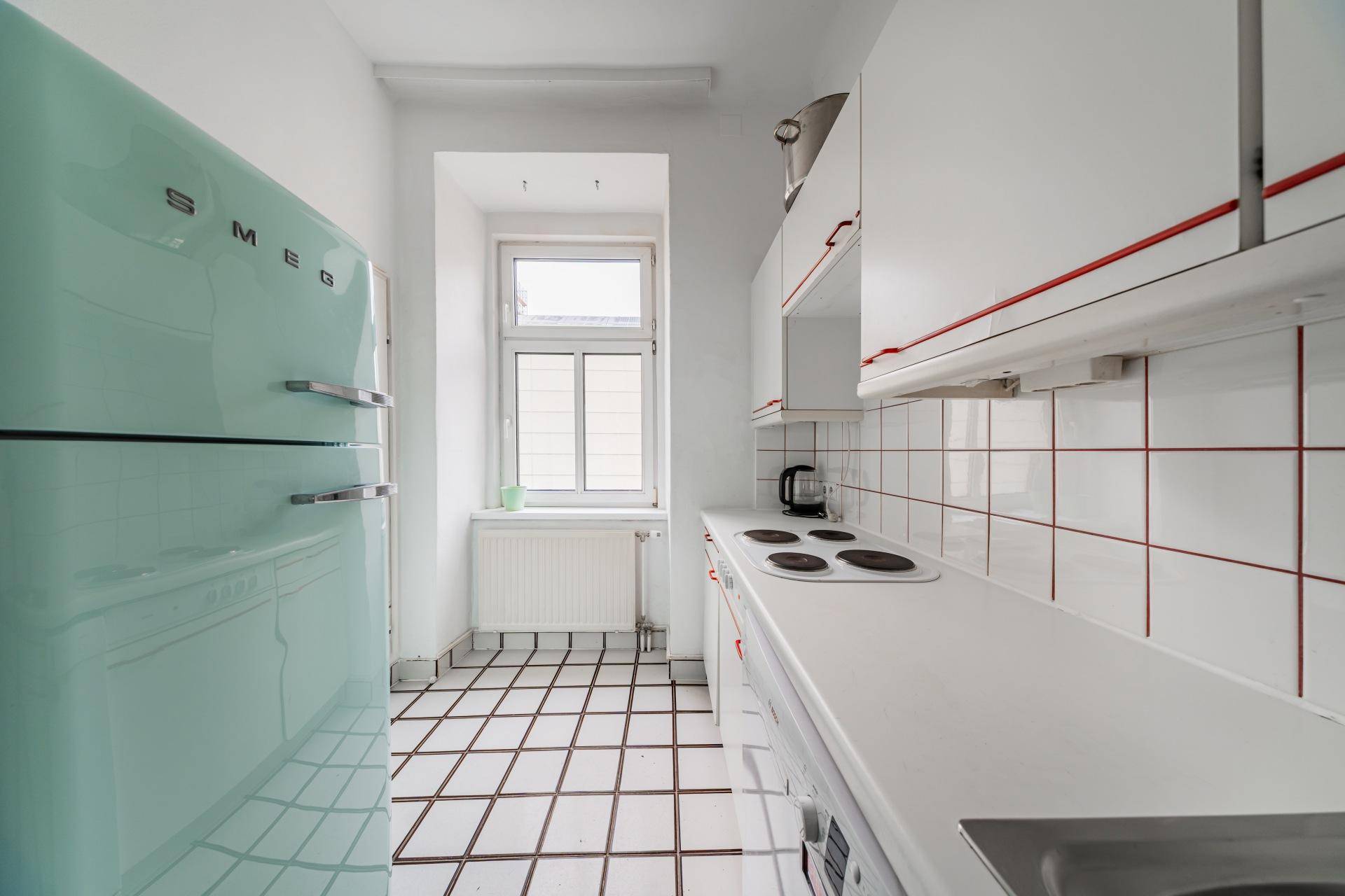 Schmale Küche mit weißen Fliesen, einem mintgrünen Kühlschrank und einem Fenster.
