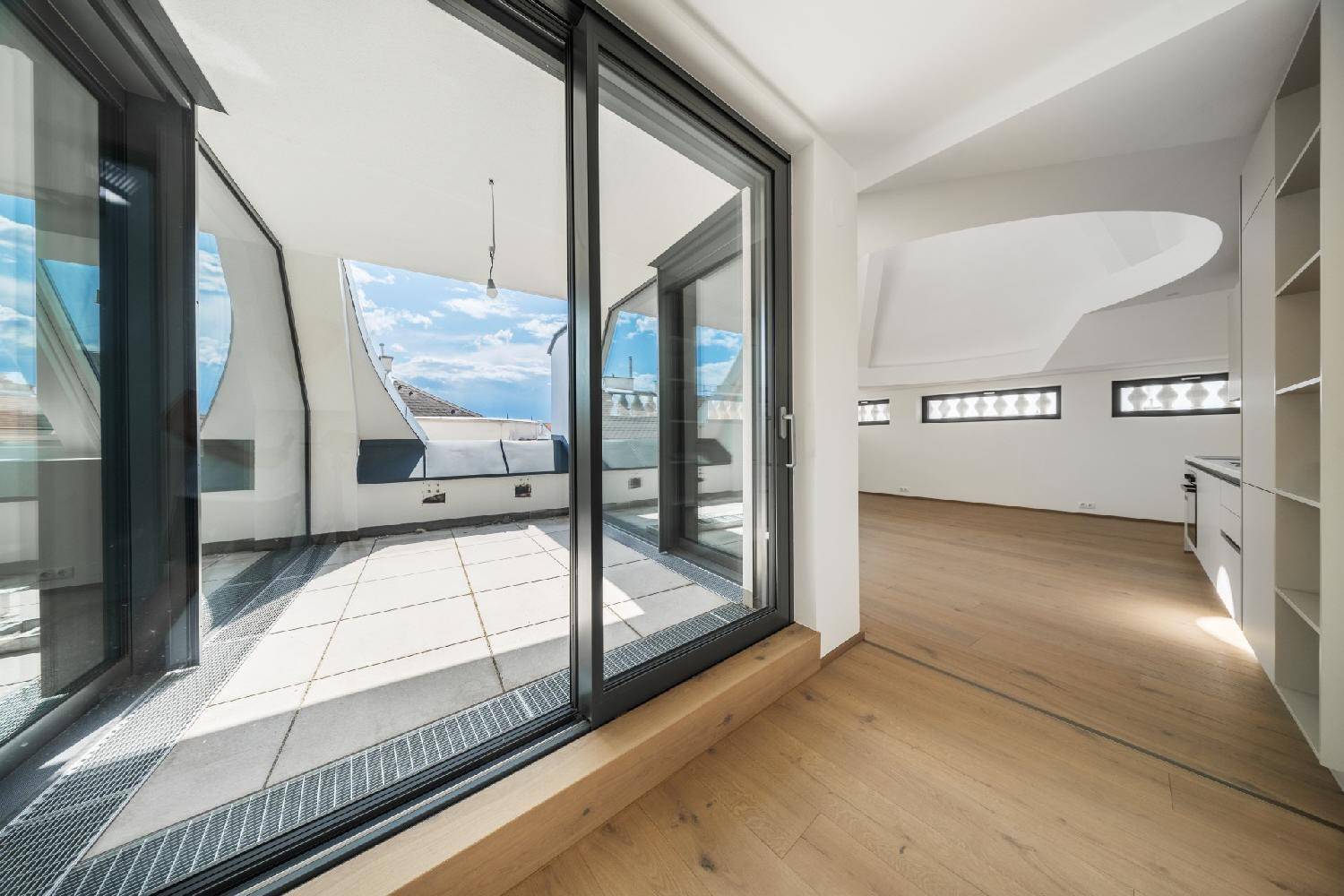 Große Glasschiebetüren öffnen den Wohnbereich zu einer sonnigen, gefliesten Dachterrasse mit Weitblick.