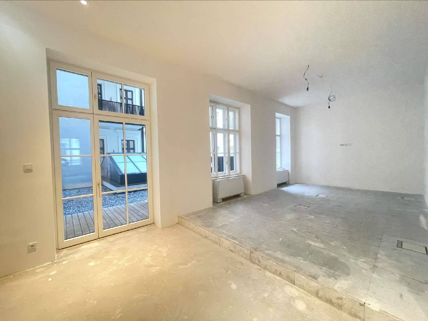 Heller Büroraum mit großen Fenstertüren zum Innenhof und Betonboden, ideal für kreative Arbeitsbereiche.