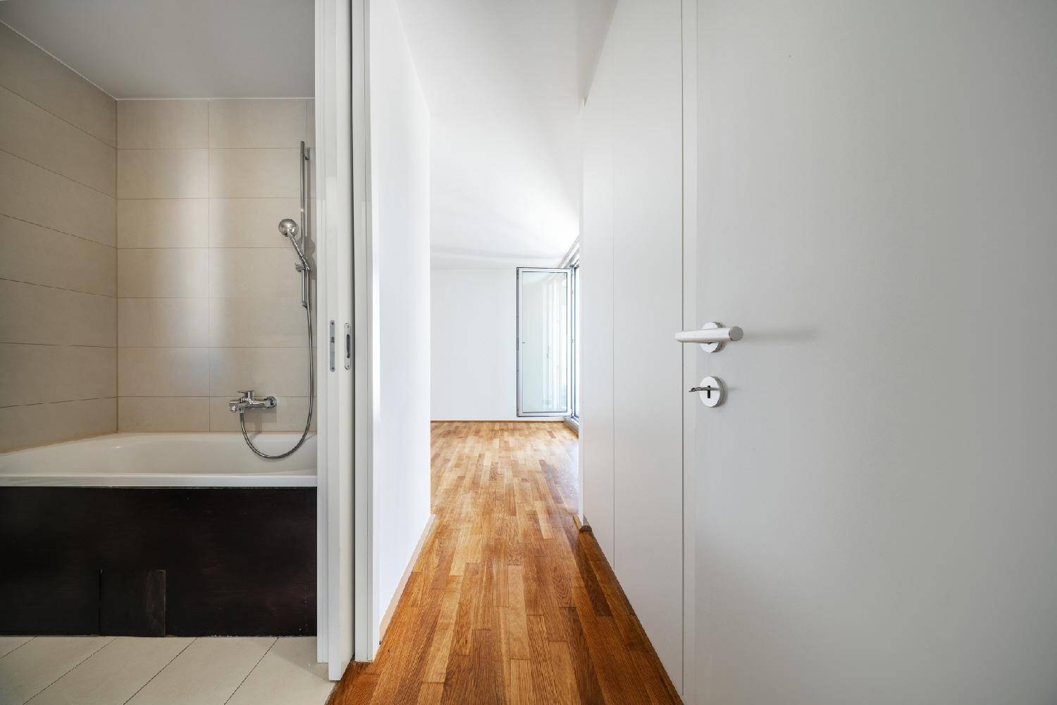 Blick vom Flur in ein Badezimmer mit Badewanne, gekennzeichnet durch Holzboden im Flurbereich.