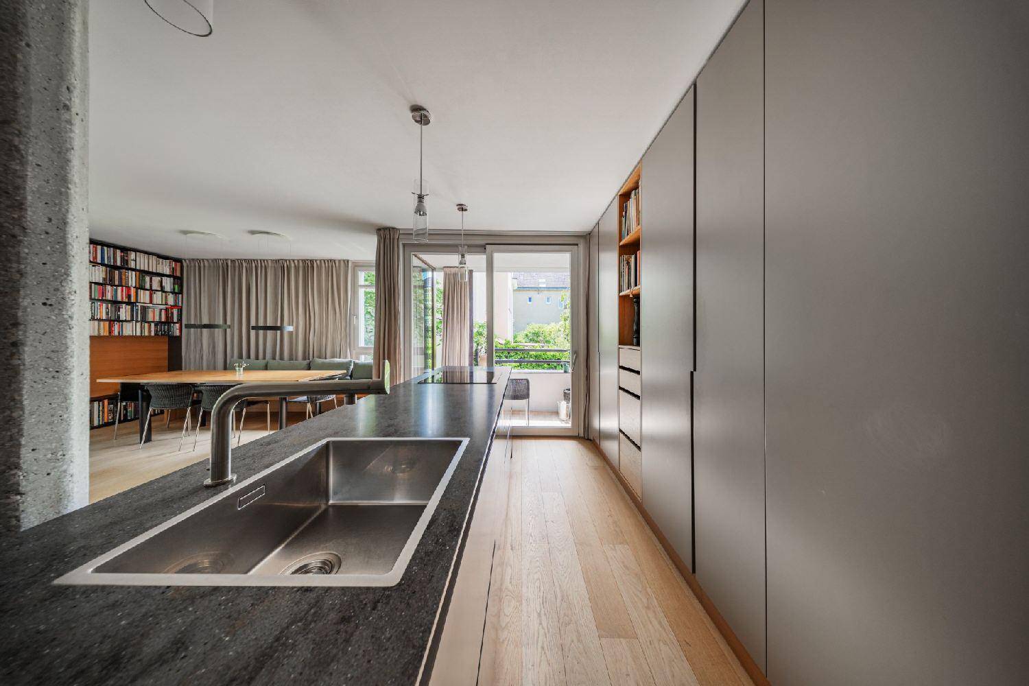 Moderne Küche mit dunkler Arbeitsplatte, integrierter Spüle und Blick in den Wohnbereich.