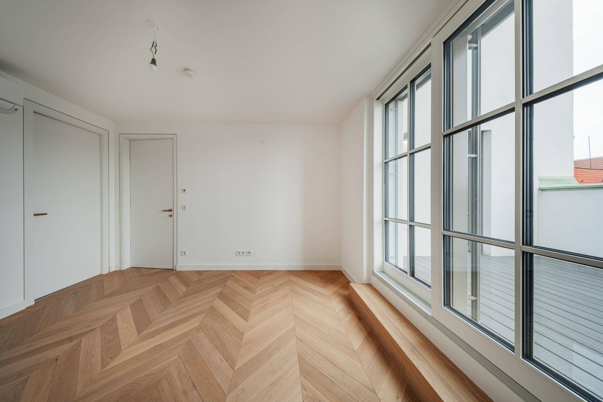 Modernes Zimmer mit Fischgrätparkett und großen Fenstern, die viel Tageslicht hereinlassen.