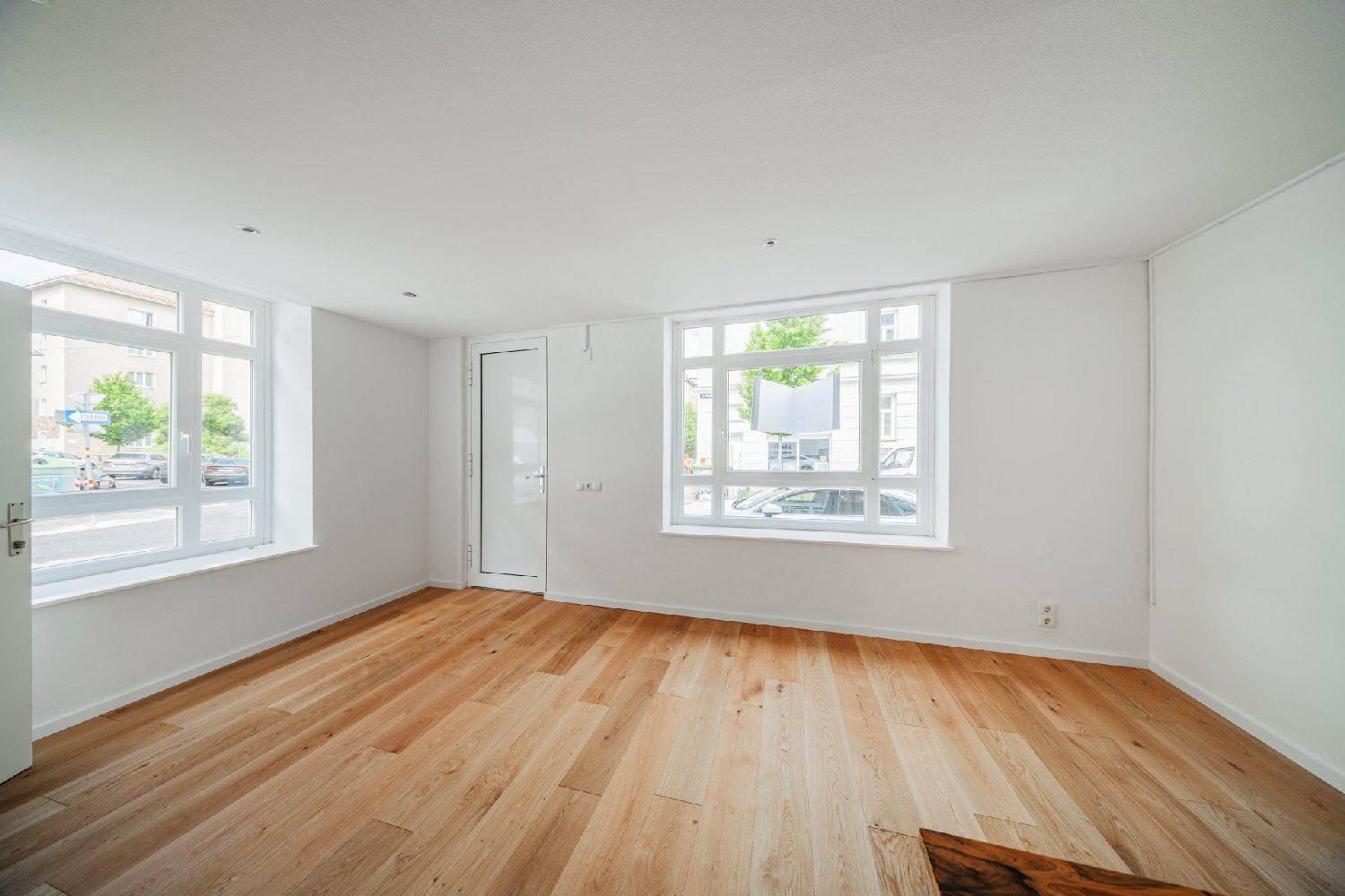 Heller Raum im Erdgeschoss mit Holzboden und großen Schaufenstern zur Straße, ideal für Ladenlokal.