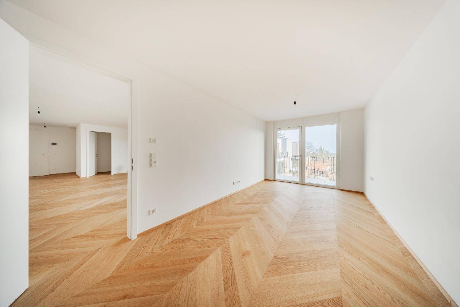 Lichtdurchflutetes Schlafzimmer mit hellem Fischgrät-Parkettboden und Zugang zu einem kleinen Balkon.