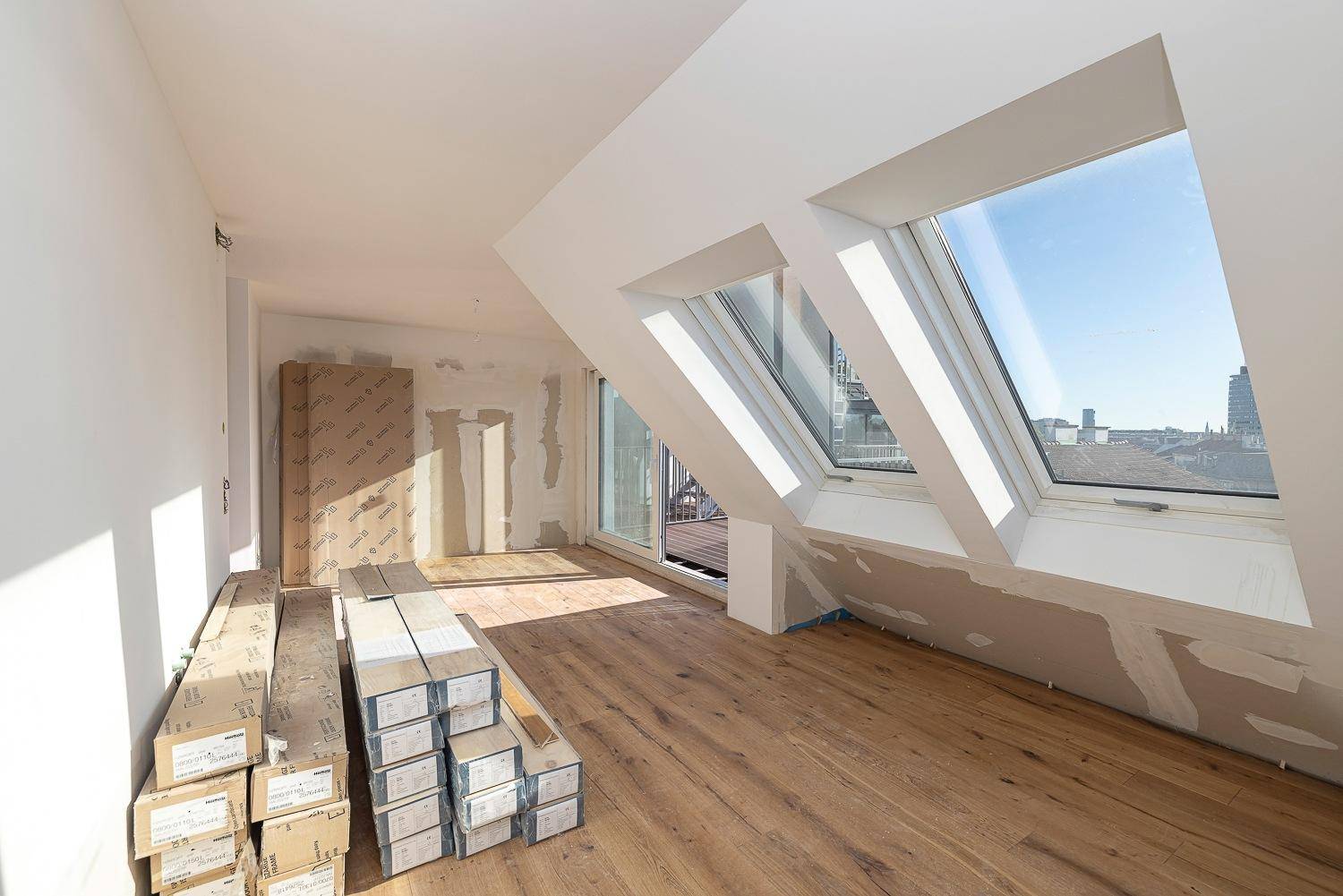 Dachgeschossraum im Bau mit Holzboden, Dachfenstern und Baumaterialien, hell und geräumig.
