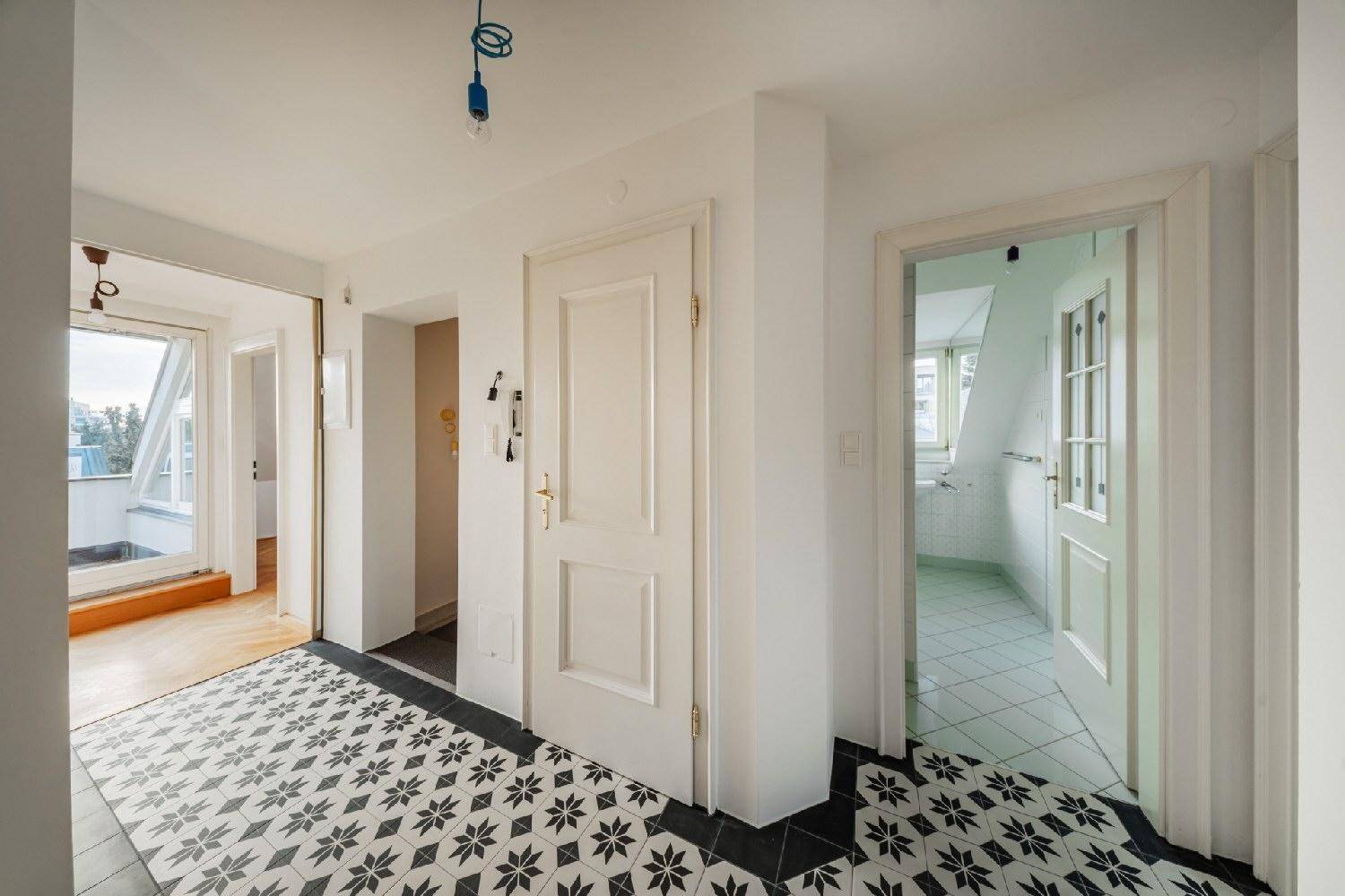 Geräumiger Flur mit gemusterten Fliesen, Zugang zum Bad und einem Balkon im Hintergrund.