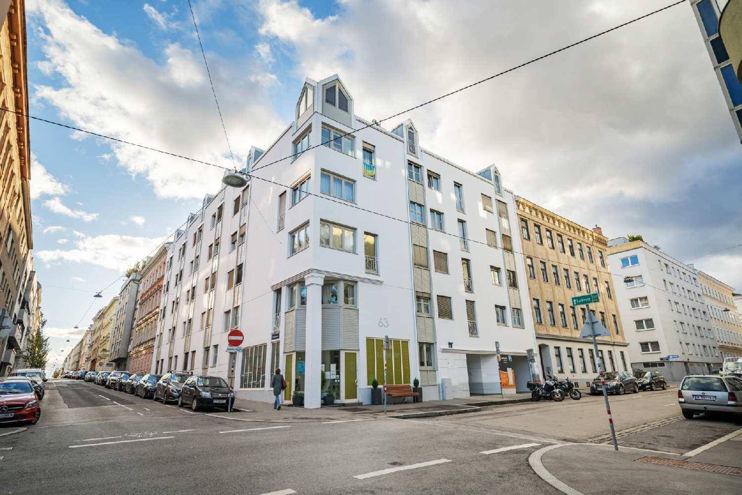 Modernes Eckgebäude in der Stadt mit weißer Fassade und vielen Fenstern an einem bewölkten Tag.