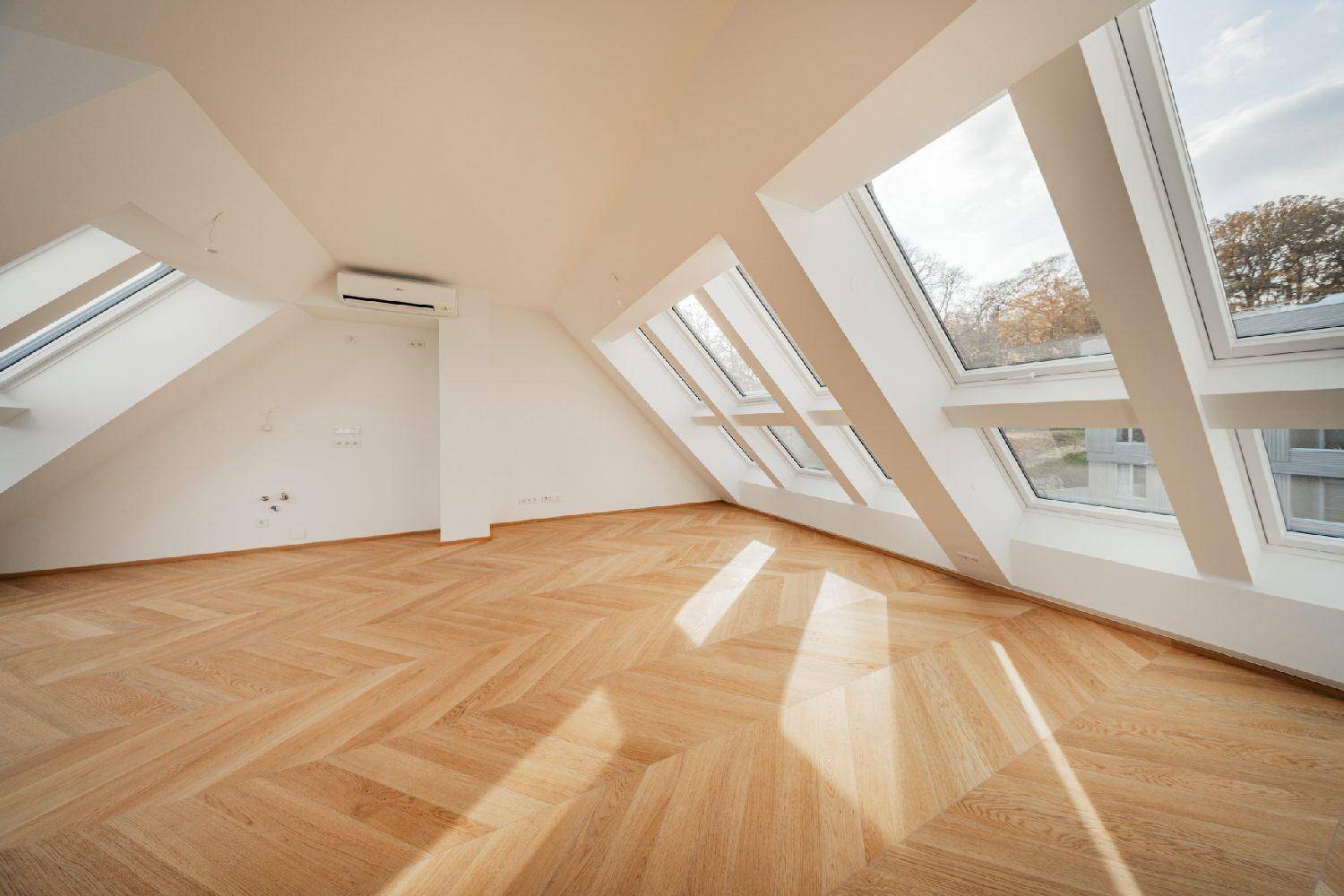Lichtdurchflutetes Dachgeschosszimmer mit schrägem Dach und elegantem Fischgrätparkettboden.