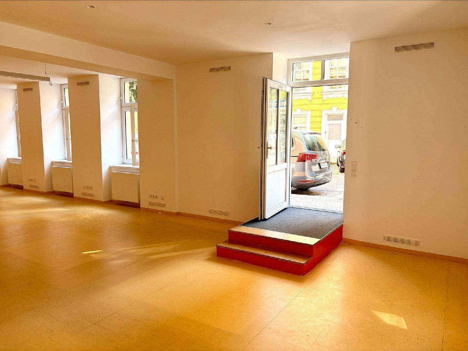 Eingangsbereich des Gewerberaums mit roten Stufen, die zur Straße führen, und viel Tageslicht.