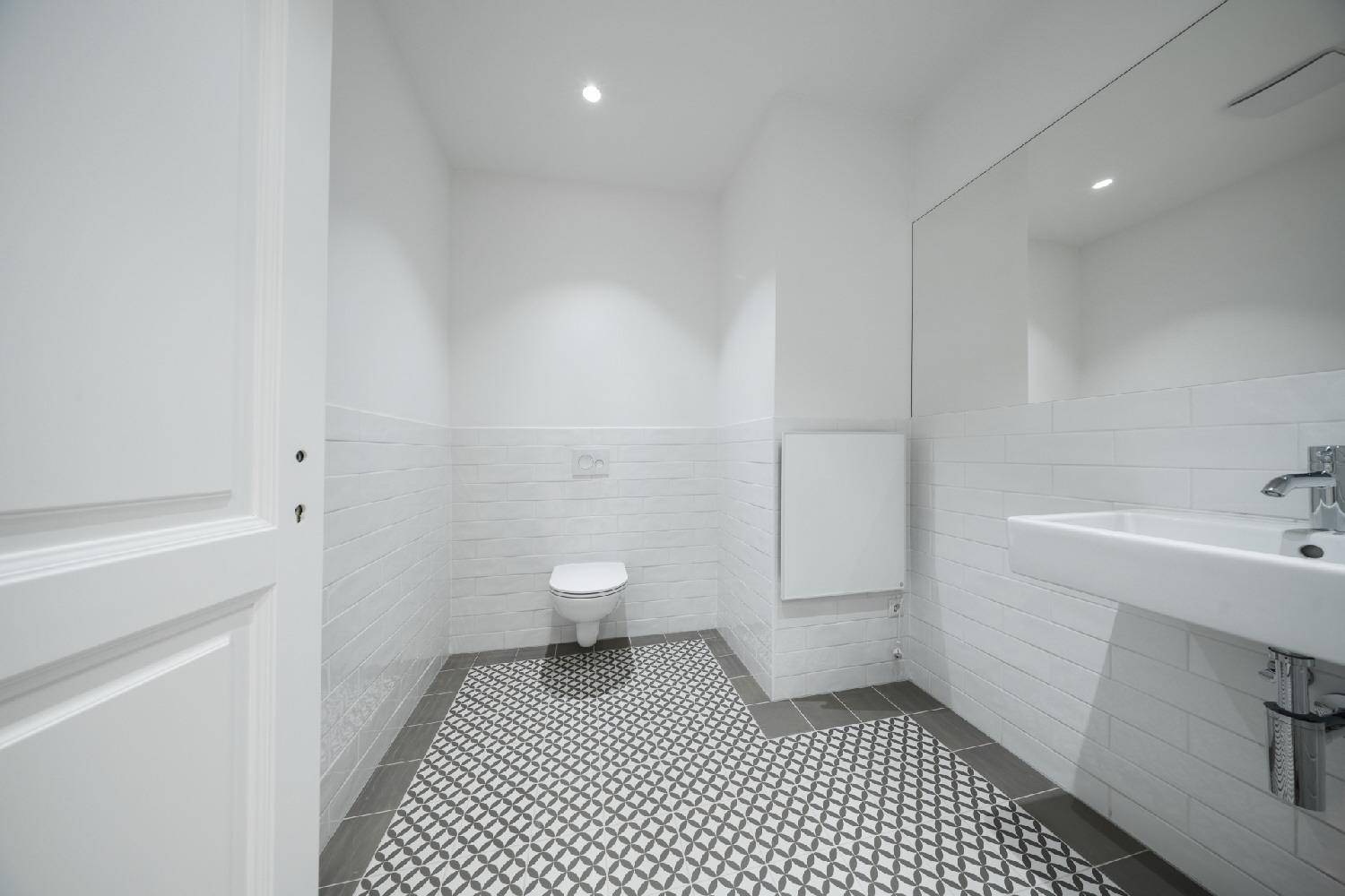 Modernes Gäste-WC mit weißen Fliesen, Waschbecken und WC, sowie gemusterten Bodenfliesen.