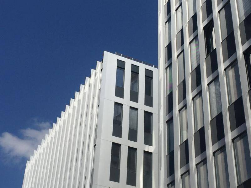 Detailansicht einer modernen Gebäudefassade mit vertikalen weißen und dunklen Elementen unter blauem Himmel.