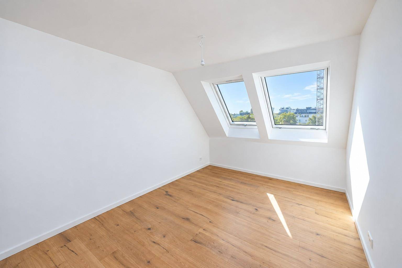 Helles Schlafzimmer mit Holzboden und schrägen Wänden, beleuchtet durch zwei Dachfenster.
