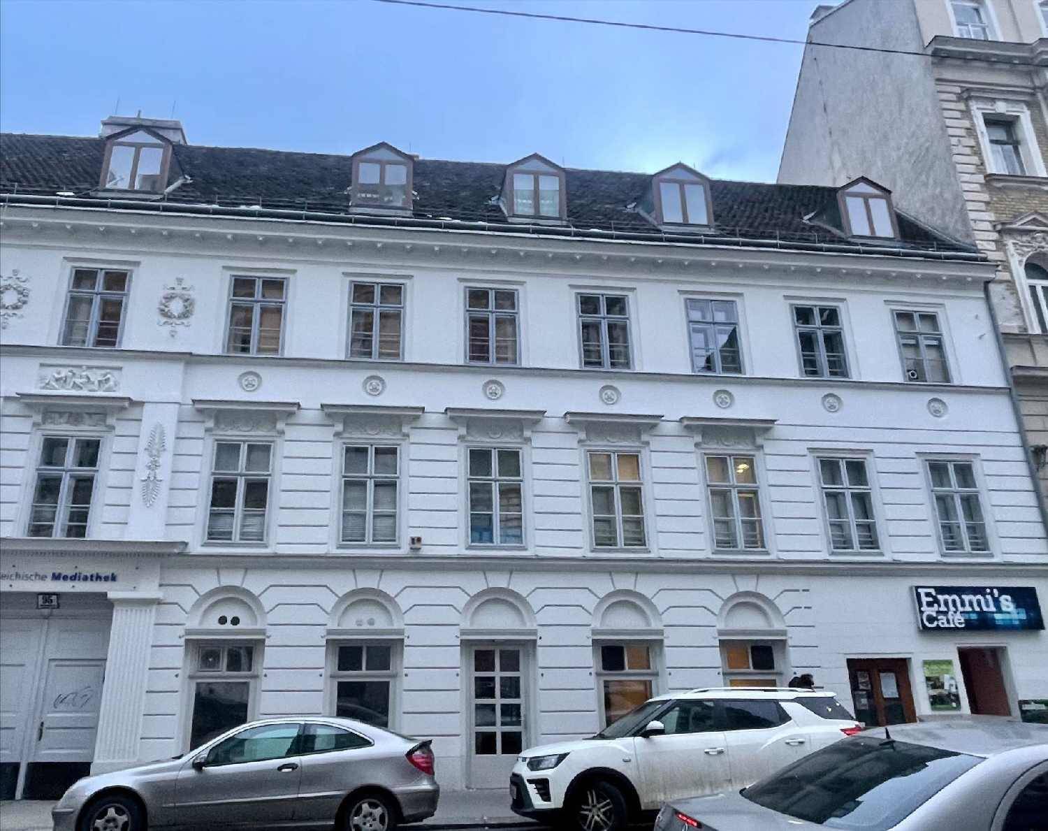 Klassische weiße Fassade eines Mehrfamilienhauses mit vielen Fenstern und Geschäften im Erdgeschoss.