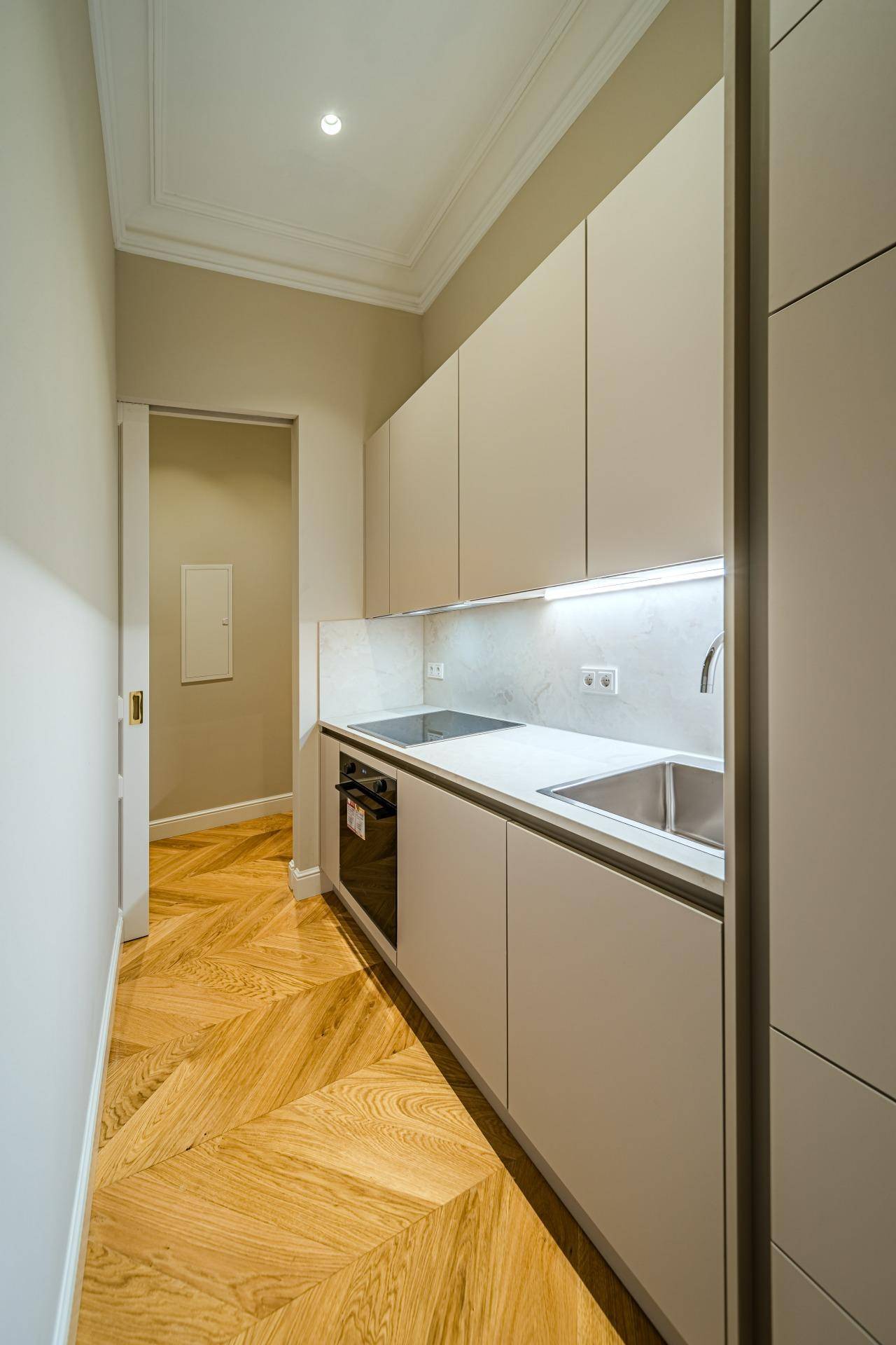 Moderne, schmale Küche mit hellen Schränken, integrierten Geräten und Fischgrätparkettboden.