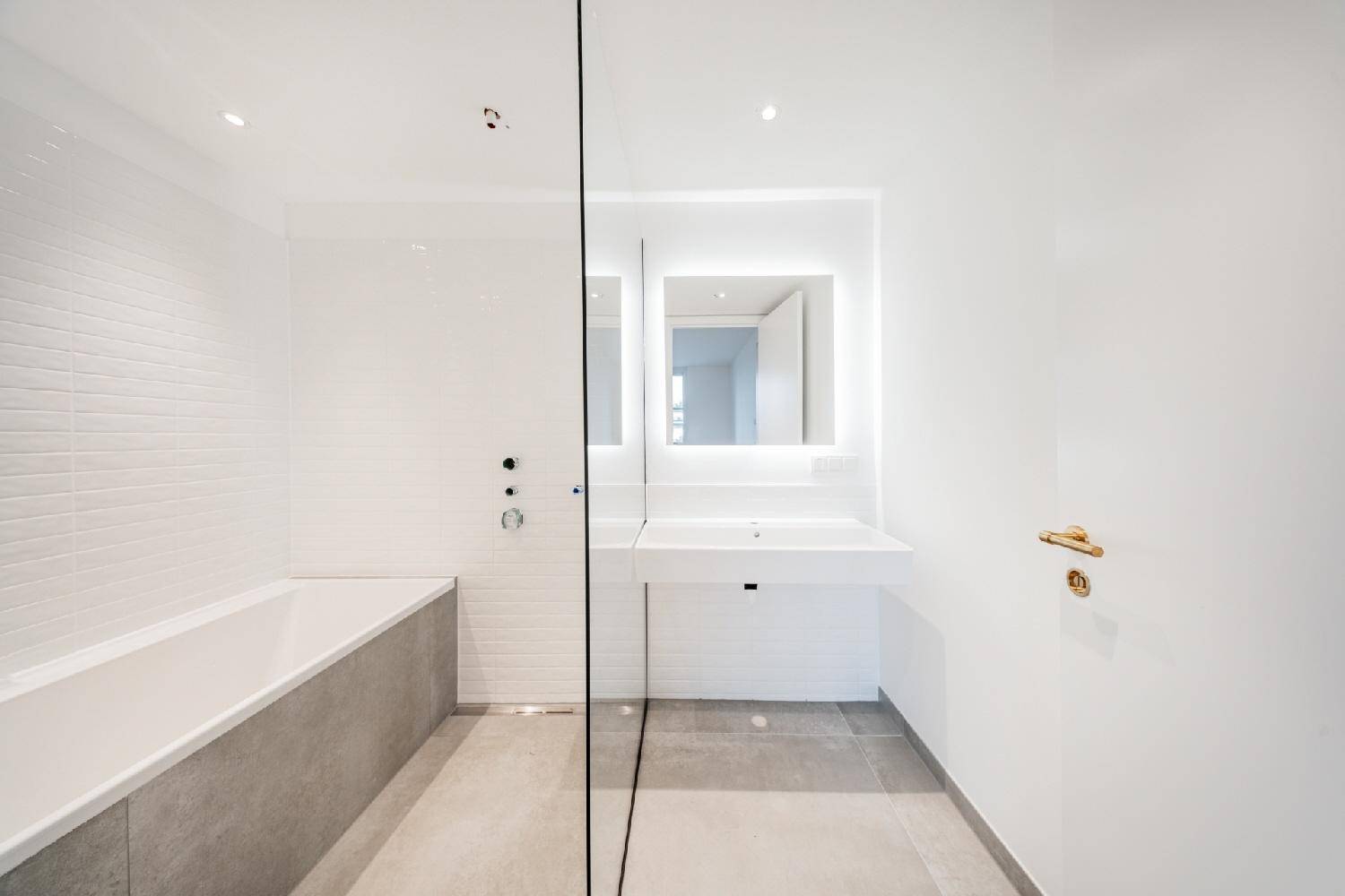 Modernes Badezimmer mit Badewanne, Dusche und beleuchtetem Spiegel über dem Waschbecken.