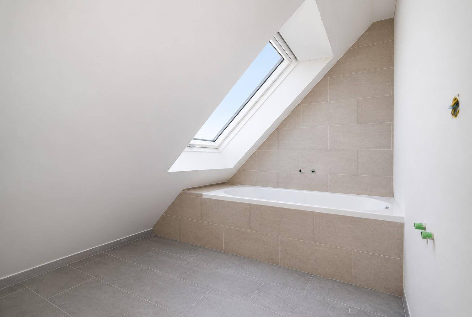 Modernes Badezimmer im Dachgeschoss mit Badewanne, Fliesen und Dachfenster.