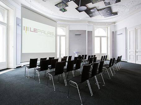 Großer Präsentationsraum mit Reihen von Stühlen, Leinwand und dekorativer Decke.