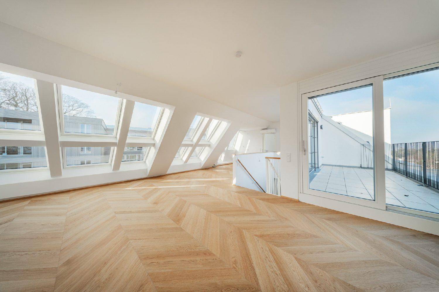 Heller Wohnbereich im Dachgeschoss mit vielen Fenstern, Parkettboden und Zugang zur Terrasse.