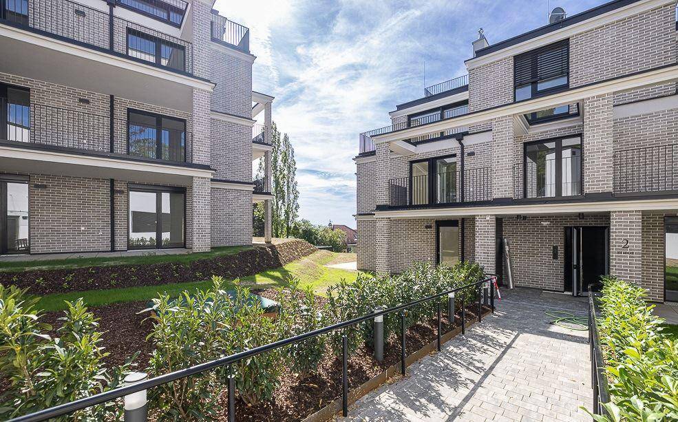 Moderne Gebäude mit heller Ziegelfassade, ebenerdigem Zugang und gepflegten Grünflächen im Außenbereich.
