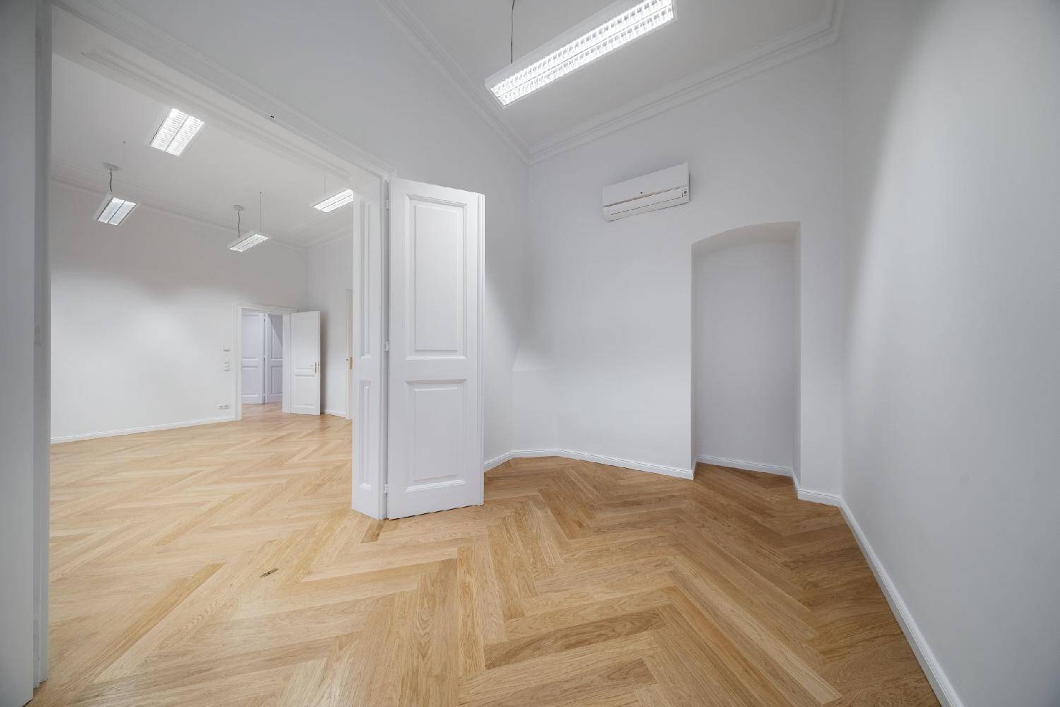 Leerer Raum mit Fischgrätparkett, weißen Wänden, Klimaanlage und einer eleganten Nische.