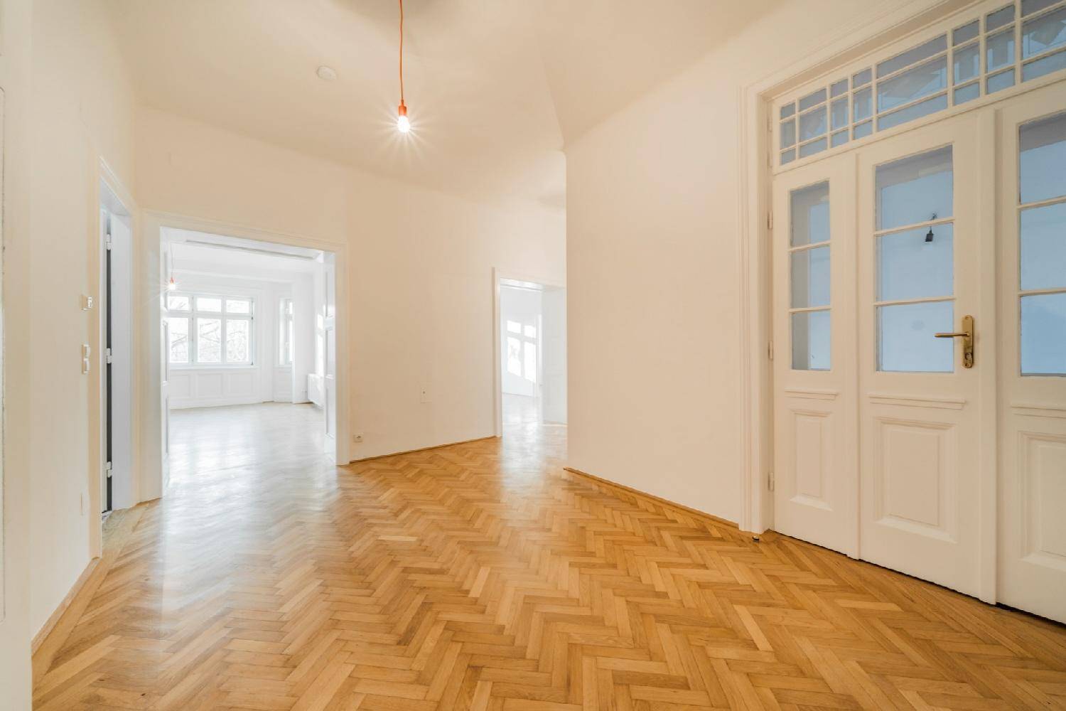 Eleganter Flur mit Fischgrätparkett und hohen Türen, der verschiedene Wohnbereiche miteinander verbindet.