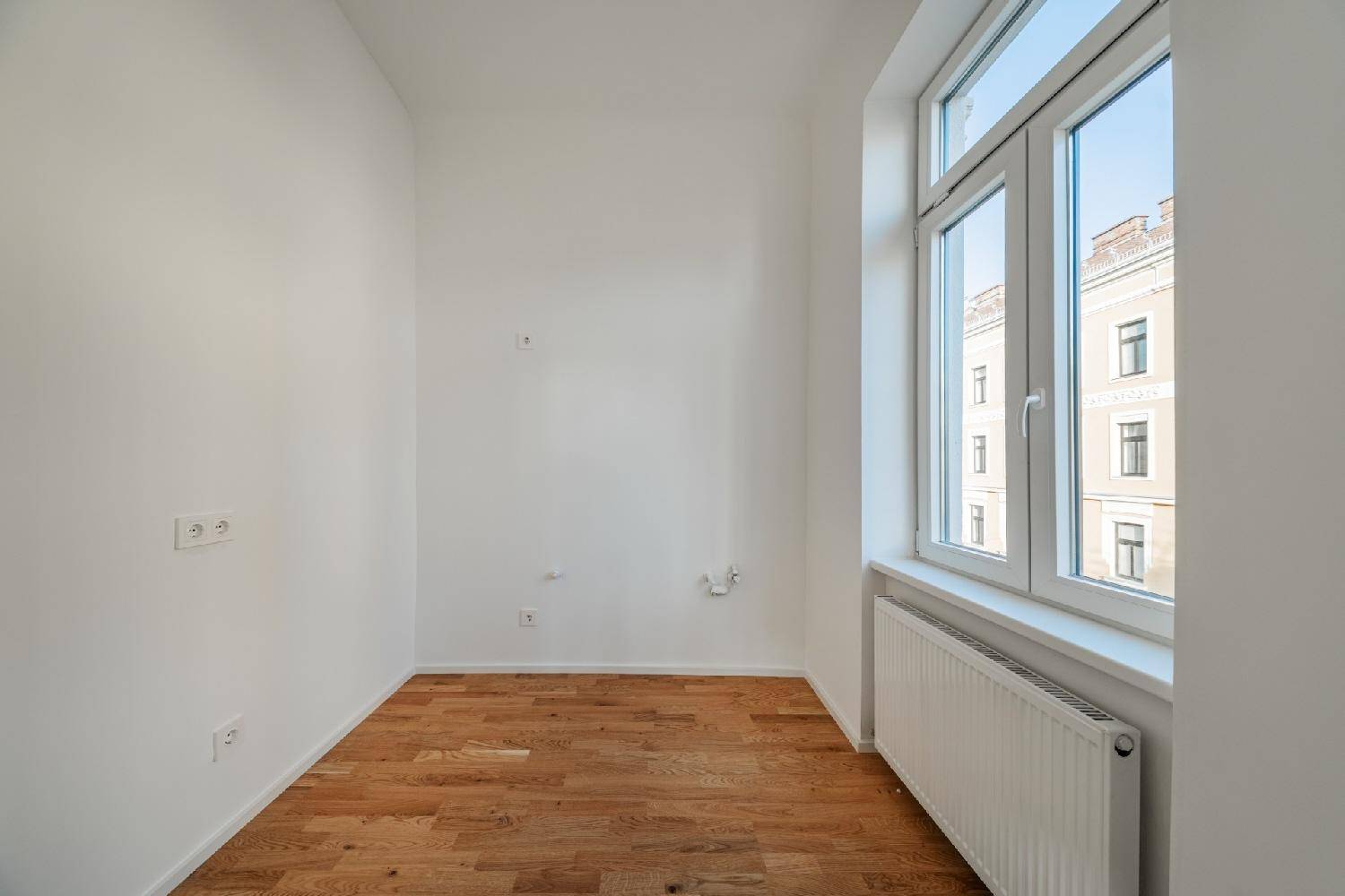 Kleineres, helles Zimmer mit Parkettboden und einem großen Fenster, ideal als Schlaf- oder Arbeitszimmer.