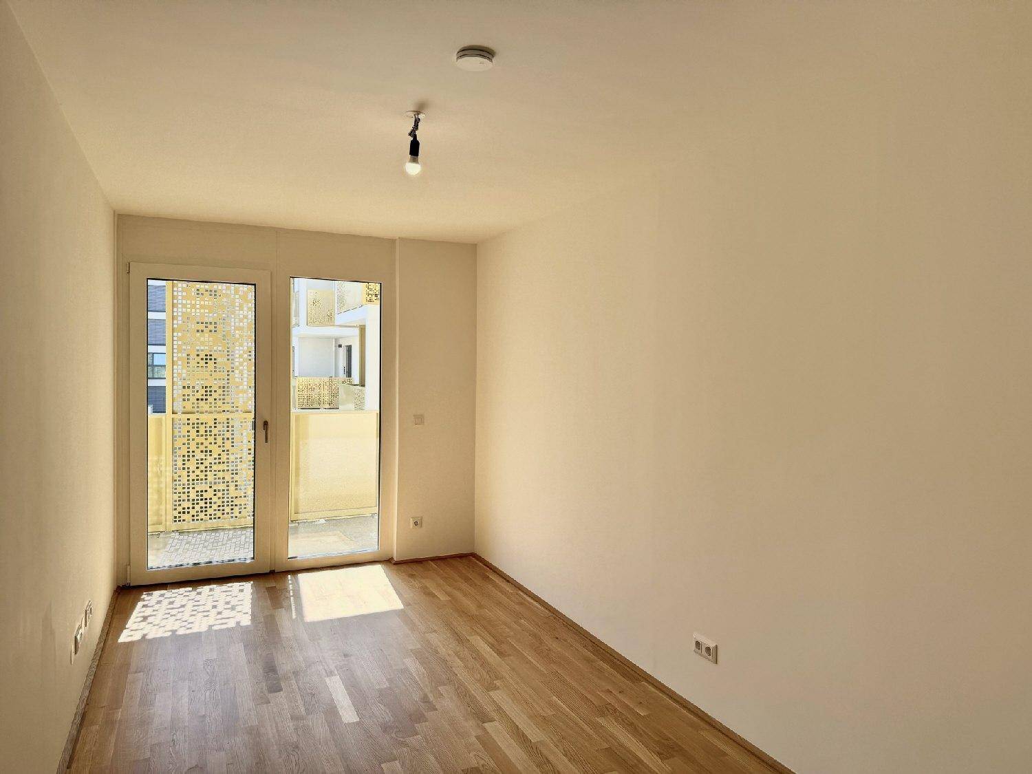 Sonniger Raum mit Parkettboden und Zugang zu einem Außenbereich, ideal als Schlafzimmer.