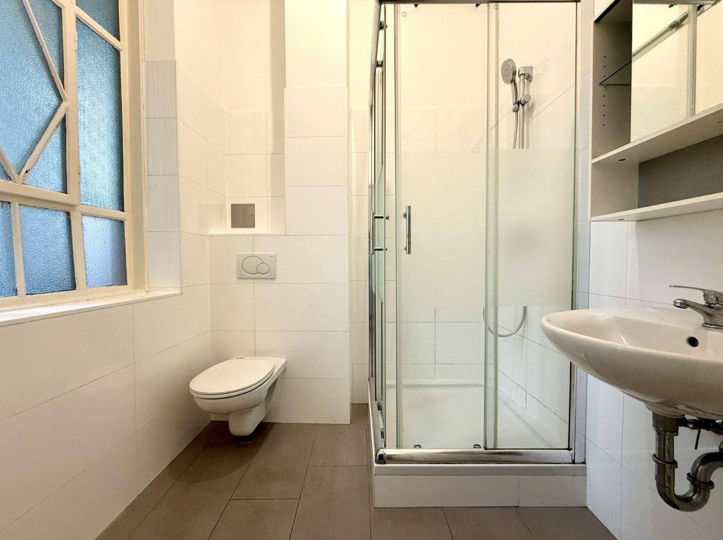 Modernes Badezimmer mit Duschkabine, WC, Waschbecken und Fenster.