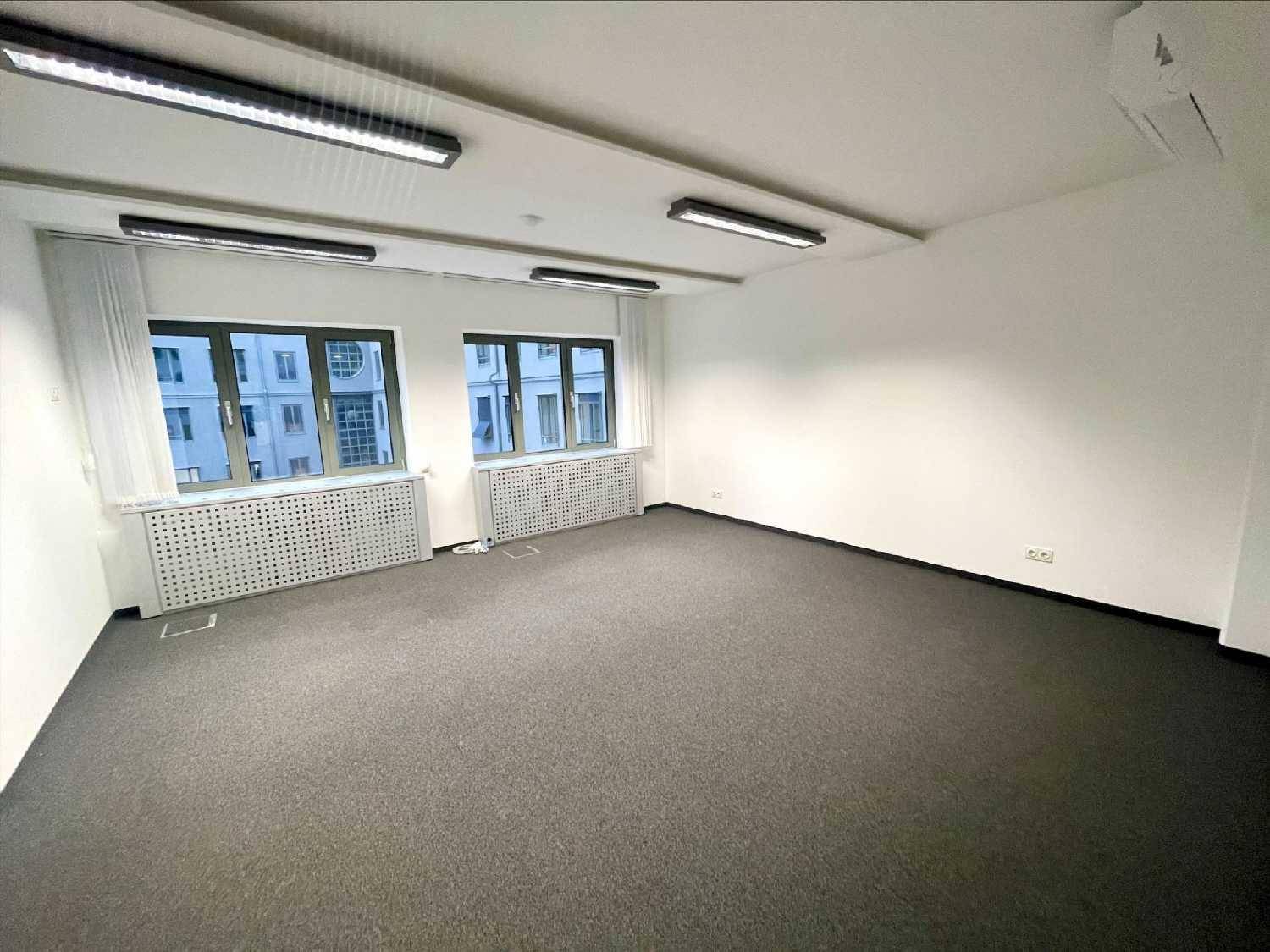 Heller Büroraum mit Teppichboden, mehreren Fenstern und moderner Deckenbeleuchtung.
