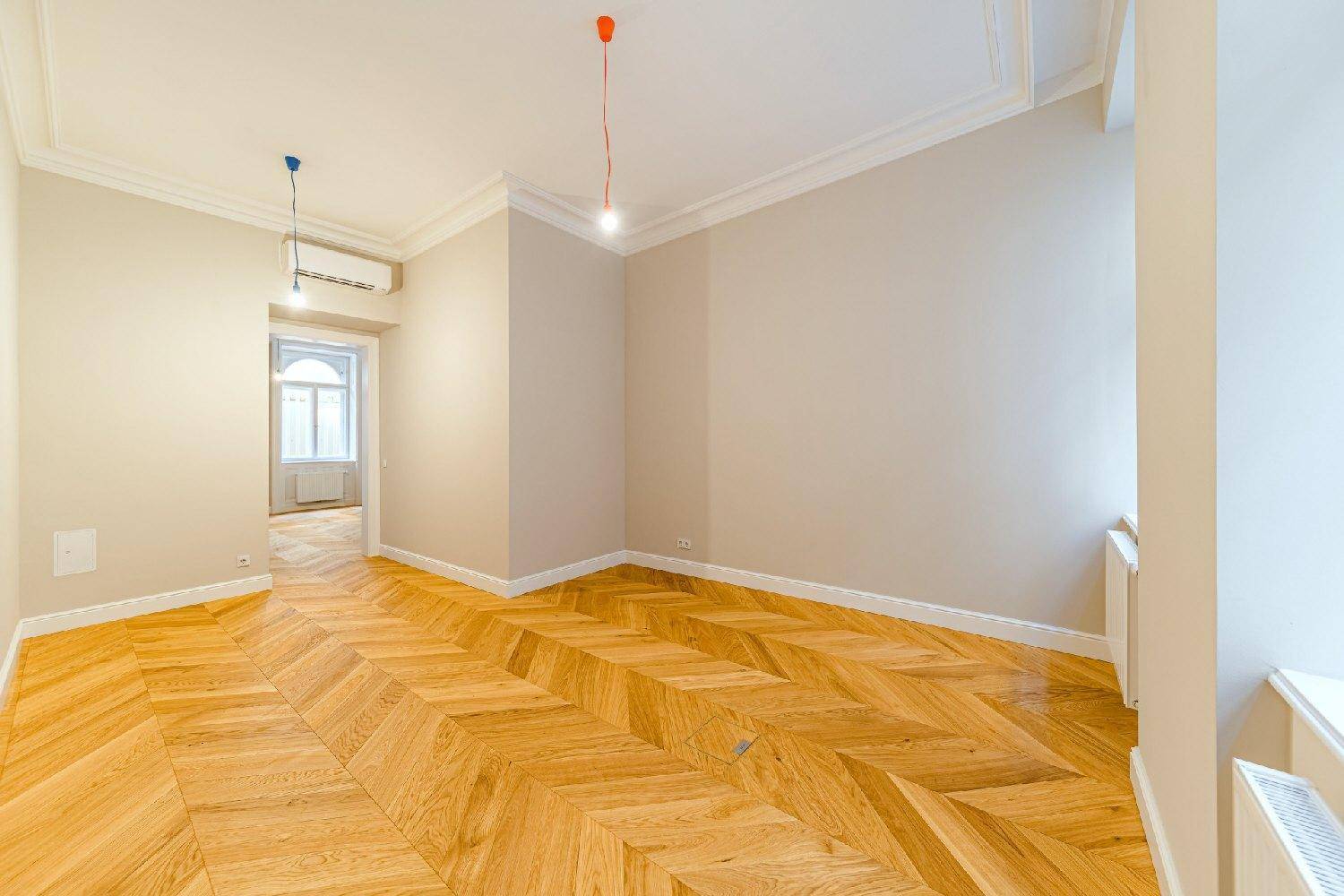 Heller Raum mit Fischgrätparkett, hohen Decken und Klimaanlage, ideal für ein Schlaf- oder Arbeitszimmer.