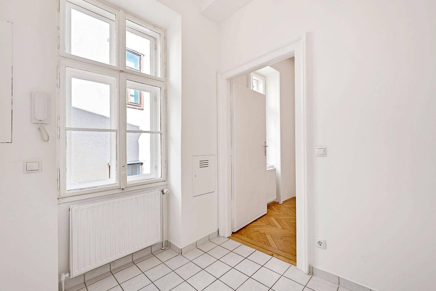 Heller Flur mit weißen Fliesen und einem Fenster, das Tageslicht in den Eingangsbereich bringt.