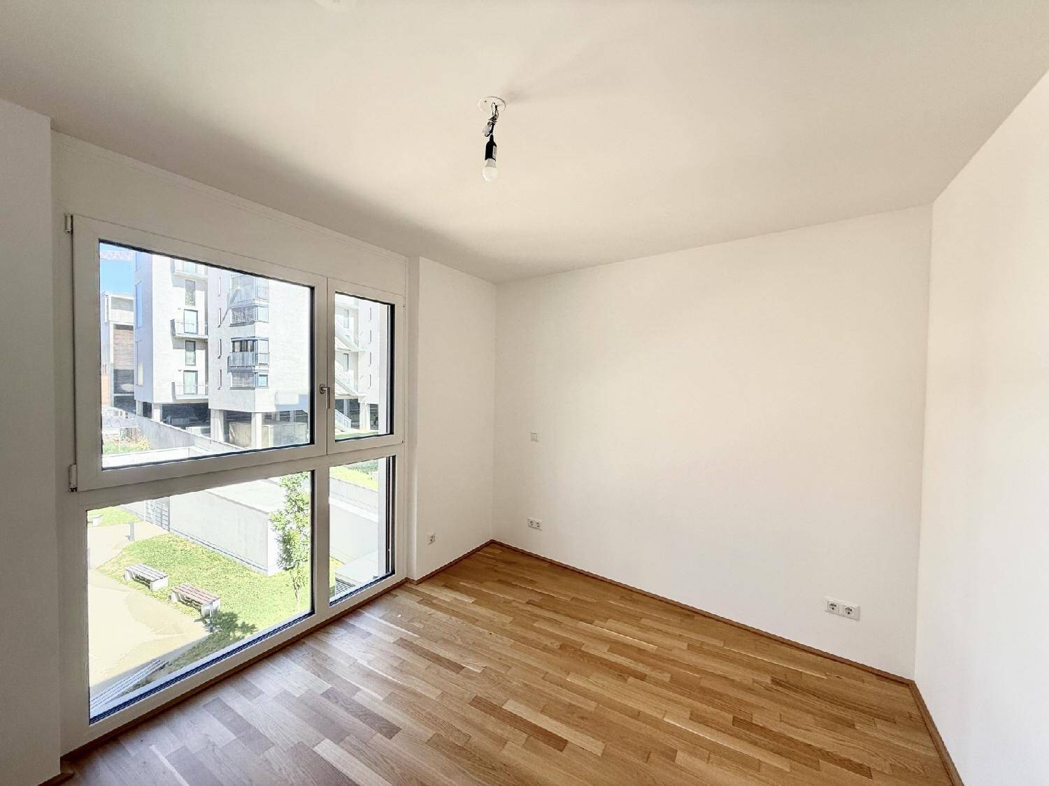 Lichtdurchflutetes Schlafzimmer mit Holzboden und Blick auf die umliegenden Gebäude.
